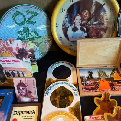 Sale Photo Thumbnail #137: Collection of Wizard of Oz memorabilia, including a wall clock, framed needlepoint artwork, a wooden shadowbox, and various themed novelty items.