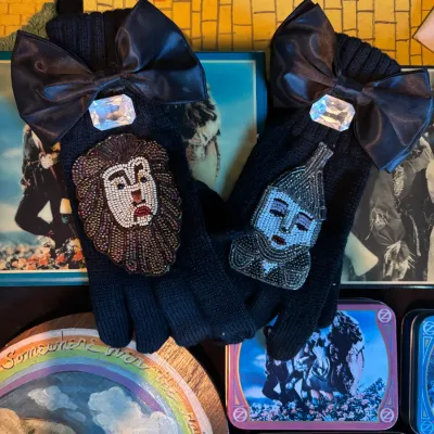 Sale Photo Thumbnail #126: Pair of black knit gloves decorated with large black faux-leather bows, clear rhinestones, and beaded patches depicting the Cowardly Lion and Tin Man from The Wizard of Oz.