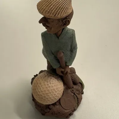 Handcrafted resin or clay golfer figurine depicting a caricature man standing over a oversized golf ball, signed and dated 1996 on the base.
