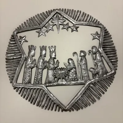 Handcrafted Haitian recycled oil drum metal wall art depicting a Nativity scene with stars and stylized sunburst border.