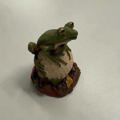 Hand-painted cast resin frog figurine resting on a golf ball with a earthy base.