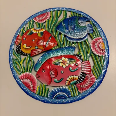 Hand-painted circular metal wall plaque depicting tropical fish and sea flora, featuring vibrant colors and embossed detail work.