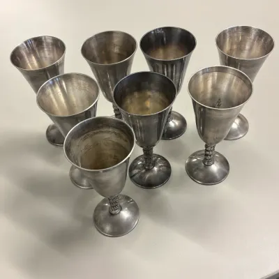 Set of eight vintage silver-plated goblets featuring decorative detailed stems and light tarnish.