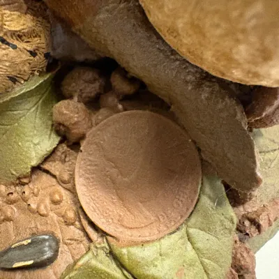 Extreme close-up detail of a textured resin figurine featuring a coin impression, leaves, and a sunflower seed motif.