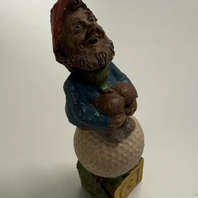 Hand-painted resin or clay gnome figurine seated on a large golf ball, featuring detailed texturing and vibrant paint finishes.