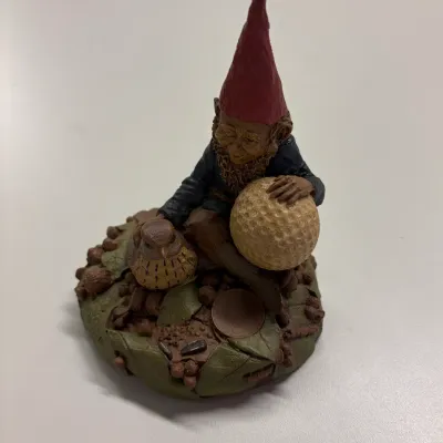 Tom Clark gnome figurine depicting a gnome holding a golf ball, crafted from resin with intricate naturalistic detail on a...