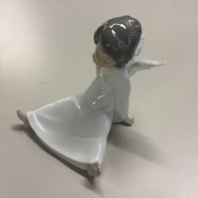 Lladro-style glazed porcelain figurine depicting a seated angel with dark hair and a white gown.