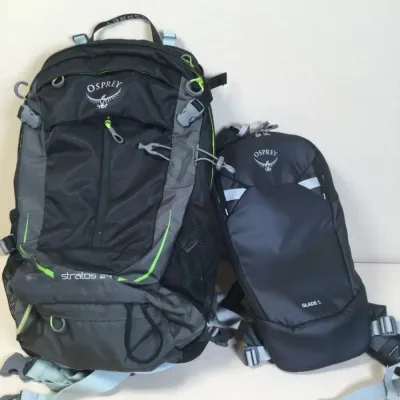 Pair of Osprey backpacks, including a Stratos 24 hiking pack in grey and lime green and a smaller Glade 5 hydration pack.