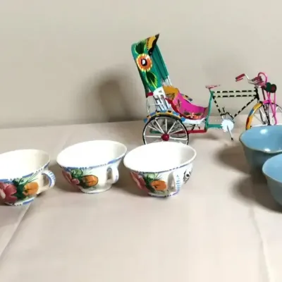 Collection of decorative tabletop items featuring four hand-painted floral teacups, three light blue ceramic bowls, and a colorful...