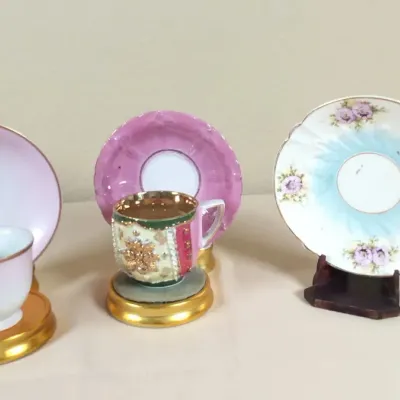 Collection of three vintage porcelain teacups and saucers, featuring floral accents, gilded rims, and ornate hand-painted details.