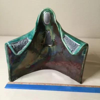 Handcrafted Raku fire cloaked figure sculpture featuring a vibrant green and iridescent raku-style glaze with detailed relief accents.