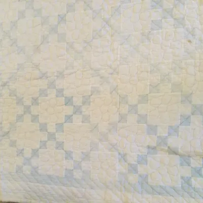 Hand-stitched vintage quilt featuring a light blue and off-white geometric chain pattern with detailed floral and cross-hatch quilting.