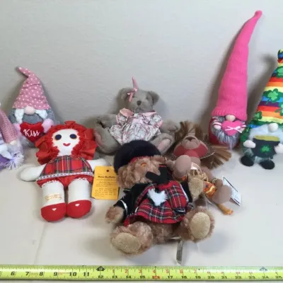 Collection of plush dolls, stuffed animals, and decorative gnomes, including a rag doll, teddy bears in outfit attire, and themed holiday...