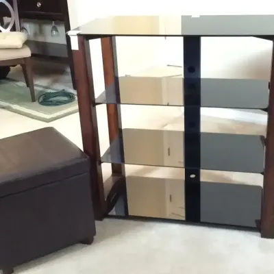 Modern dark wood media audio rack with tempered glass shelves alongside a brown leather storage ottoman.