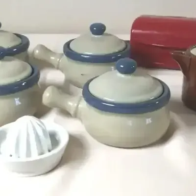 Collection of ceramic kitchenware including four lidded French onion soup bowls with handles, a brown pitcher, a white citrus reamer, and...