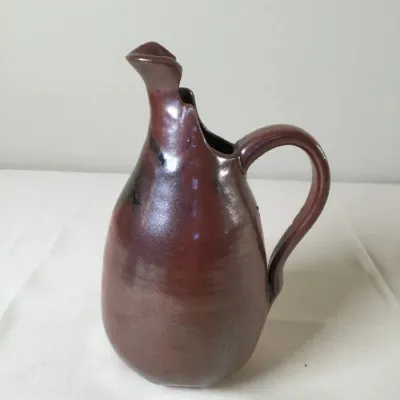 Handcrafted studio pottery pitcher featuring a rich metallic brown glaze and an organic pinched spout design.