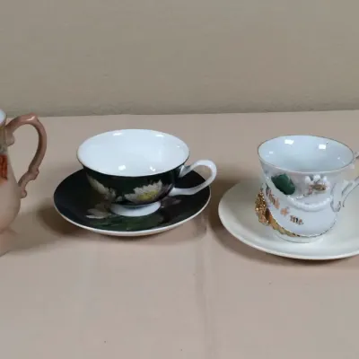 Trio of vintage porcelain teacups, including a hand-painted grape motif mug, a black and white floral cup with matching saucer, and a...