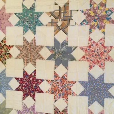 Handmade vintage patch quilt featuring a star pattern made from assorted patterned fabric scraps against an off-white background.