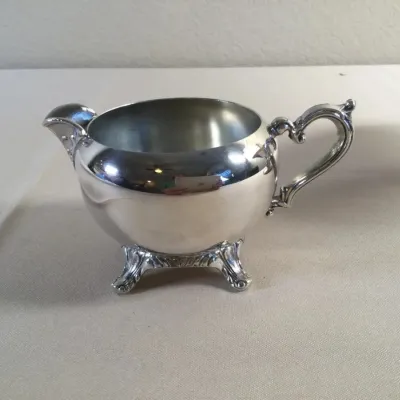 Vintage silver-plated creamer featuring an ornate scroll handle and four detailed footed legs.