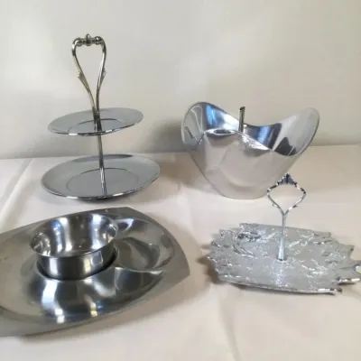 Collection of polished metal serveware, including a two-tiered tray, a chip-and-dip platter, a modern freeform bowl, and a single-tiered...