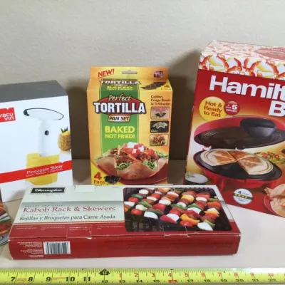 Assortment of boxed kitchen gadgets, including a Hamilton Beach quesadilla maker, Vacu Vin pineapple slicer, Perfect Tortilla pan set,...