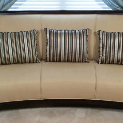 Contemporary curved armless sofa upholstered in beige fabric with dark wood trim, includes three striped accent pillows.