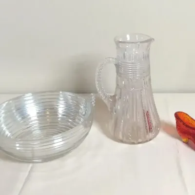 Collection of vintage glassware items including a clear ribbed oval dish with handles, a tall pressed glass pitcher, and a red amberina...