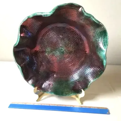 Iridescent studio Raku fire pottery bowl with a scalloped edge, featuring concentric ridges and a deep purple and green metallic glaze.