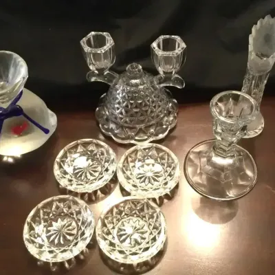 Collection of clear pressed glass tableware including a set of starburst coasters, candlesticks, a small bud vase, and a clear glass fish...