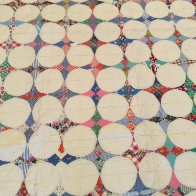Handmade patchwork quilt featuring a Cathedral Window or snowball block pattern with multicolored fabric accents and cream circles.