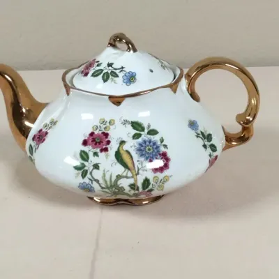 Vintage porcelain teapot featuring a bird and floral motif with heavy gold gilded accents on the handle, spout, rim, and lid finial.
