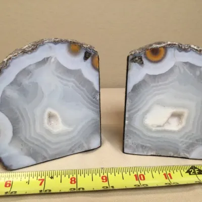 Pair of polished agate geode bookends featuring gray and white banding with small orange orb accents, shown next to a measuring tape for...