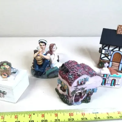 Collection of decorative miniature resin and ceramic figurines, featuring cottage houses, a small trinket box, and a seated couple.