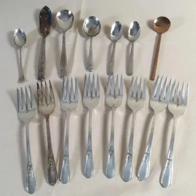 Assorted vintage silver-plated flatware, including various spoons, butter servers, and matching dinner forks with floral detail.