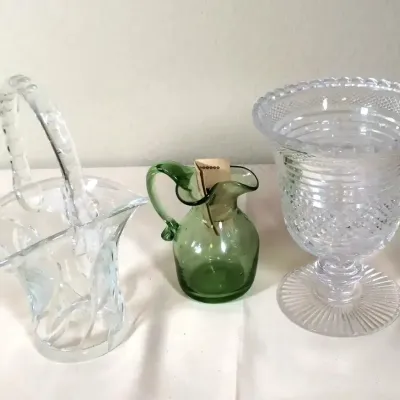 Trio of vintage glassware featuring a clear cut-glass handle basket, a small green blown-glass pitcher, and a heavy cut-crystal footed...
