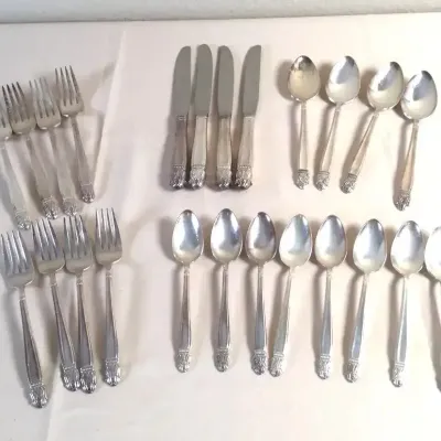 Vintage silver-plated flatware set featuring dinner forks, butter knives, soup spoons, and teaspoons with ornate handles.