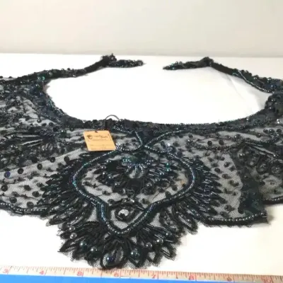 Intricately beaded black mesh collar attachment featuring sequin accents and iridescence, shown with a measuring tape.