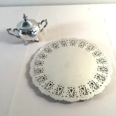 Vintage silver-plated serving set, featuring a small covered sugar bowl with scrolled handles and a round tray with a pierced, lace-style...
