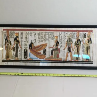 Framed Egyptian papyrus painting depicting figures, deities, and hieroglyphics, displayed in a long black frame.