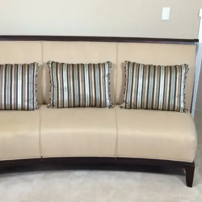 Contemporary curved bench-style sofa with dark wood trim, beige upholstery, and three striped accent pillows.