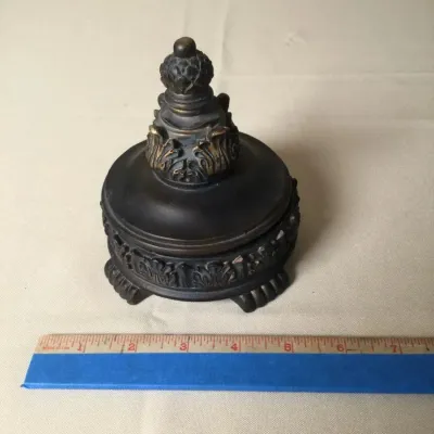 Ornate dark bronze or heavy cast metal trinket box with a pineapple finial, acanthus leaf relief details, and claw feet.