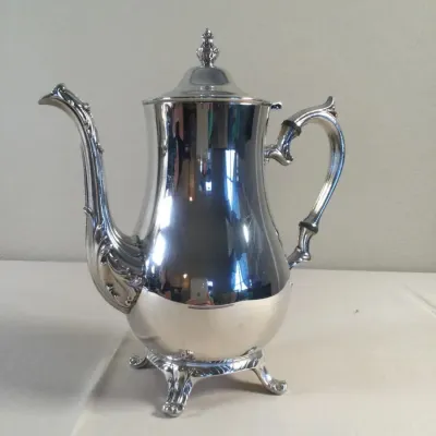 Polished silver-plated coffee pot with ornamental scroll spout, decorative feet, and insulated handle rings.