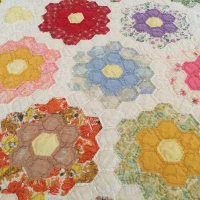 Handmade Grandmother's Flower Garden pattern quilt featuring colorful hexagonal floral rosettes on a white background, likely...