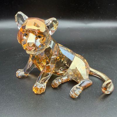 Sale Photo Thumbnail #45: Swarovski crystal tiger cub figurine in amber and clear faceted crystal, depicted in a resting pose.
