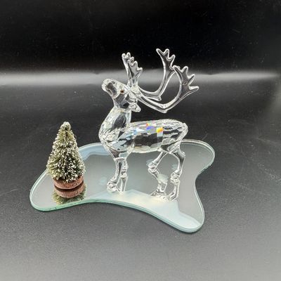 Sale Photo Thumbnail #23: Swarovski crystal reindeer figurine standing on an irregular mirrored base beside a miniature frosted bottle brush tree.