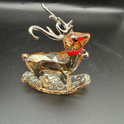 Sale Photo Thumbnail #16: Swarovski crystal rocking reindeer figurine in golden shadow crystal with silver-tone antlers and a red collar with a jingle bell.