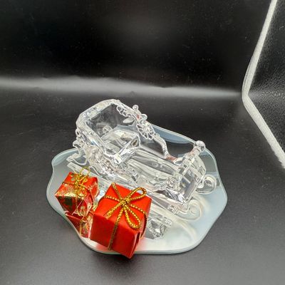 Sale Photo Thumbnail #24: Swarovski Santa sleigh figurine displayed on a mirror base alongside two small wrapped gift accessories.
