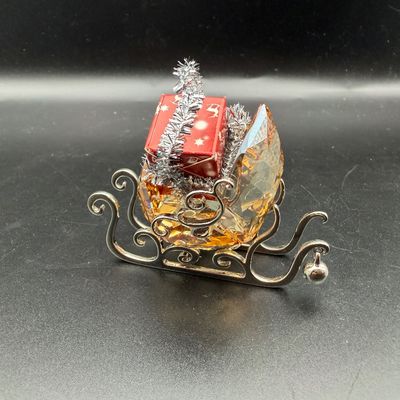 Sale Photo Thumbnail #17: Swarovski crystal Santa's sleigh figurine, featuring an amber-tinted faceted crystal body on a silver-tone runner frame, loaded with miniature wrapped presents.