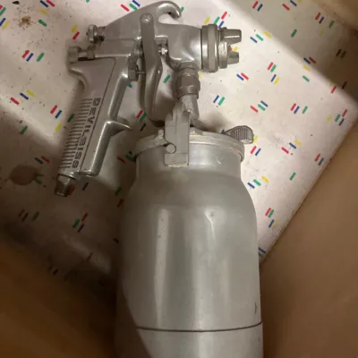 Vintage DeVilbiss pneumatic paint spray gun with attached metal canister, showing light wear from use.