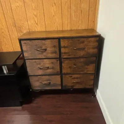 Industrial-style six-drawer dresser featuring rustic faux-wood fabric drawers, a black metal frame, and a solid wood grain top.